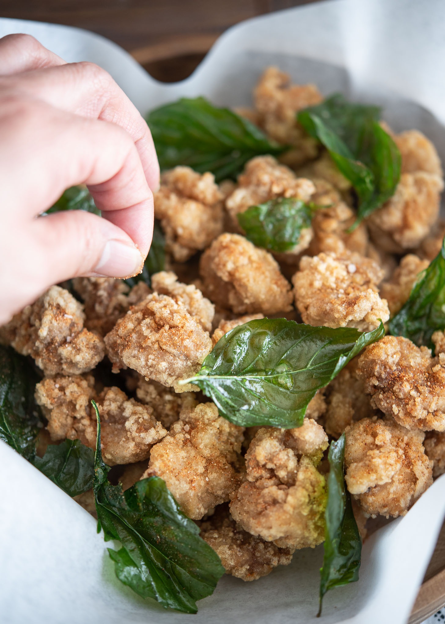 Chicken seasoning mix sprinkling over fried golden brown popcorn-sized chicken and Thai basil.