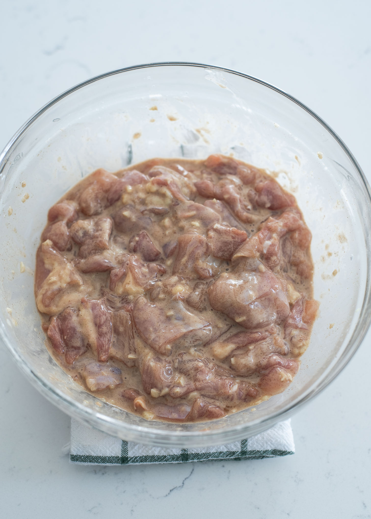 Chicken thigh pieces seasoned in a mixing bowl.