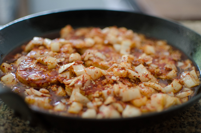 Tofu slices and spicy seasoning is combined in a skillet.