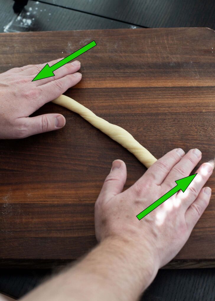 Both hands are rolling each end of dough rope in opposite direction.
