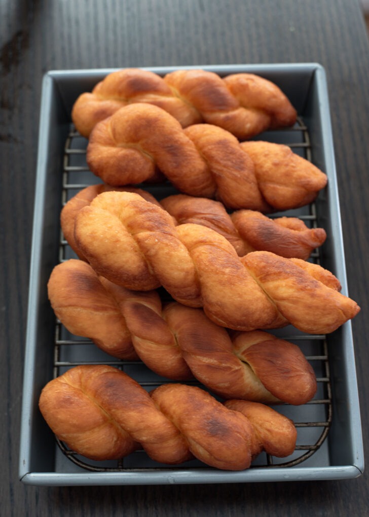 Fried twisted donuts are placed on a wired rack to drip extra oil from the surface.