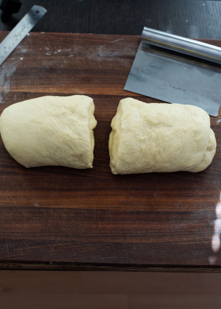 The donut dough is divided in half using a dough cutter on the wooden board.